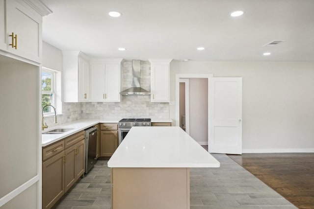 kitchen with sink, a center island, wall chimney range hood, hardwood / wood-style floors, and appliances with stainless steel finishes