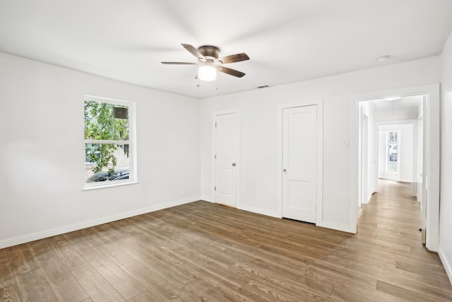 unfurnished bedroom with ceiling fan, wood-type flooring, and two closets