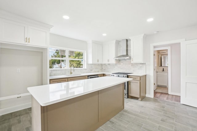 kitchen with sink, wall chimney exhaust hood, a kitchen island, white cabinetry, and stainless steel appliances