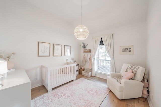 bedroom featuring light wood-type flooring, a crib, and an inviting chandelier