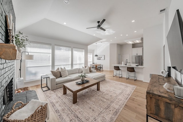 living room with lofted ceiling, sink, a brick fireplace, ceiling fan, and light hardwood / wood-style floors