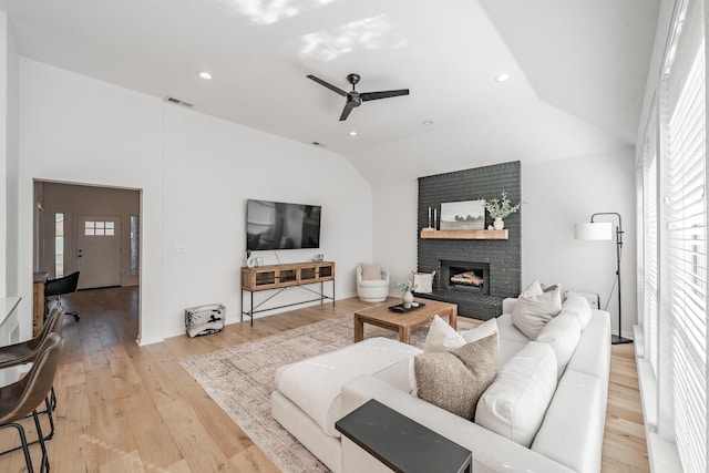 living room with ceiling fan, a fireplace, vaulted ceiling, and light wood-type flooring