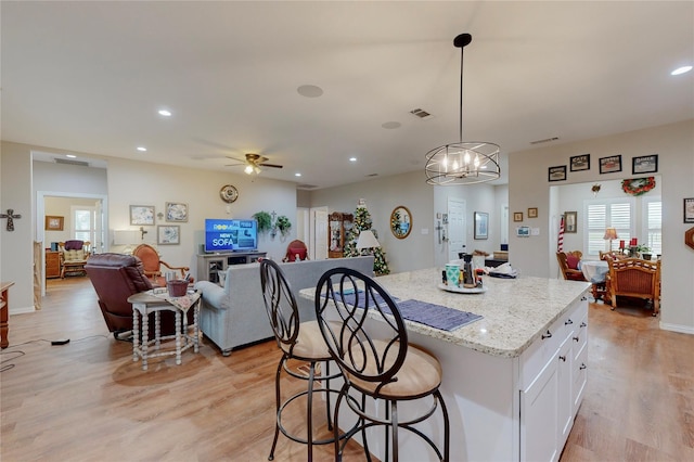 kitchen with decorative light fixtures, a kitchen island, light stone countertops, ceiling fan with notable chandelier, and white cabinets