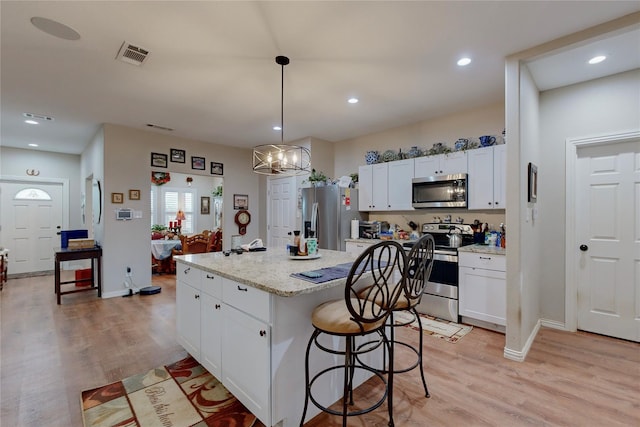 kitchen featuring a kitchen island with sink, hanging light fixtures, stainless steel appliances, and white cabinets