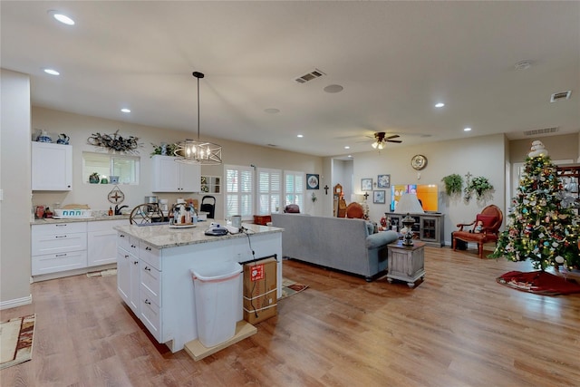 kitchen featuring pendant lighting, white cabinetry, light stone countertops, a kitchen island, and light wood-type flooring