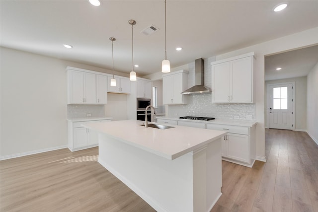 kitchen featuring wall chimney exhaust hood, built in microwave, sink, white cabinetry, and an island with sink