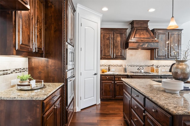 kitchen with appliances with stainless steel finishes, light stone counters, dark brown cabinetry, and premium range hood