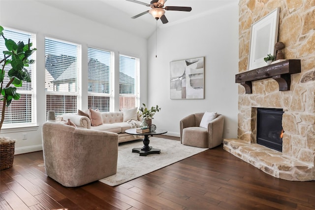 living room featuring a stone fireplace, vaulted ceiling, crown molding, ceiling fan, and dark wood-type flooring