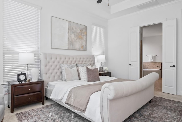 bedroom featuring ensuite bath, ceiling fan, a tray ceiling, and ornamental molding