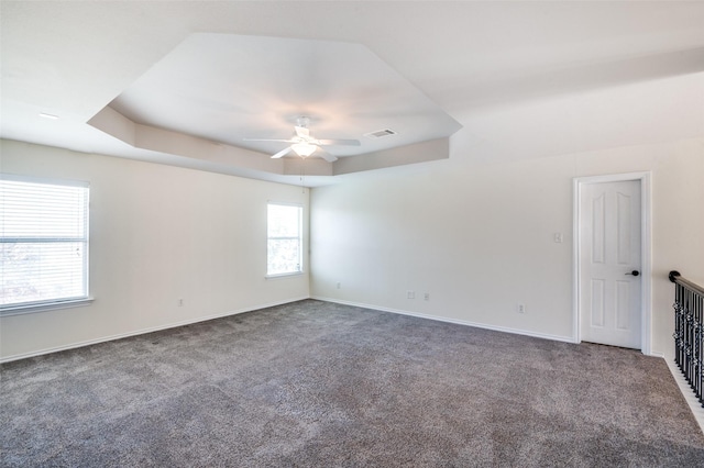 carpeted spare room with a raised ceiling and ceiling fan