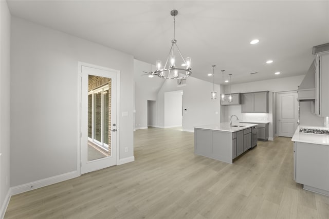 kitchen featuring light wood-type flooring, a kitchen island with sink, a chandelier, gray cabinets, and hanging light fixtures