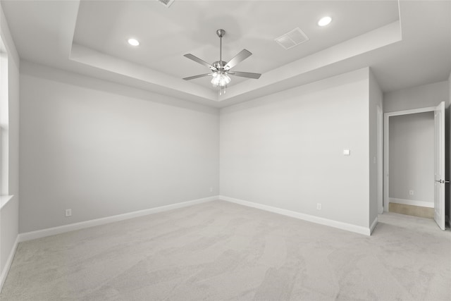 unfurnished room with a raised ceiling, ceiling fan, and light colored carpet