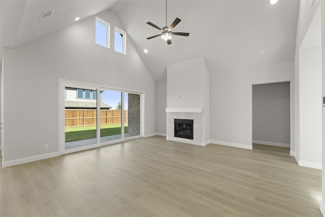 unfurnished living room featuring ceiling fan, light wood-type flooring, a fireplace, and a high ceiling