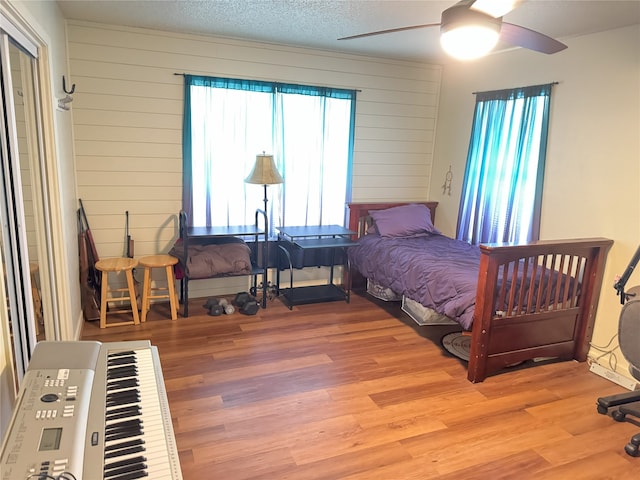 bedroom with a textured ceiling, light wood-type flooring, ceiling fan, and wooden walls