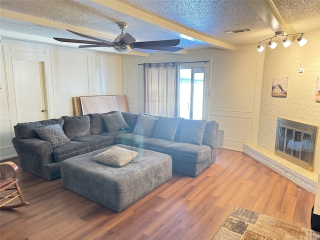 living room with hardwood / wood-style flooring, ceiling fan, a fireplace, a textured ceiling, and beamed ceiling