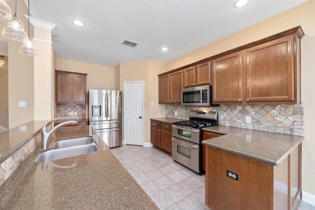 kitchen with appliances with stainless steel finishes, decorative light fixtures, sink, and dark stone countertops