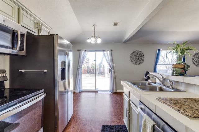 kitchen featuring stainless steel appliances, sink, cream cabinets, an inviting chandelier, and hanging light fixtures