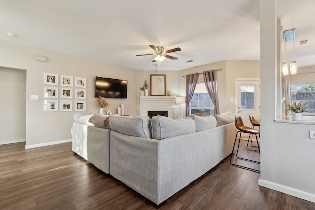 living room with a brick fireplace, ceiling fan, and dark wood-type flooring