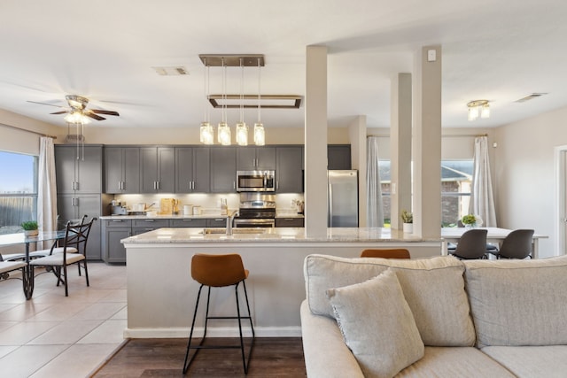 kitchen featuring pendant lighting, ceiling fan, gray cabinets, light stone countertops, and stainless steel appliances