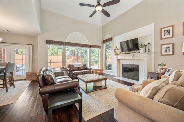 living room featuring a tile fireplace, ceiling fan, dark wood-type flooring, and a wealth of natural light