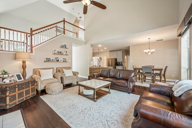 living room with ceiling fan with notable chandelier, dark wood-type flooring, and a high ceiling