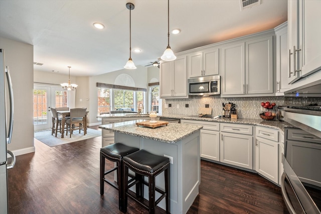 kitchen featuring light stone countertops, sink, hanging light fixtures, a kitchen island, and appliances with stainless steel finishes