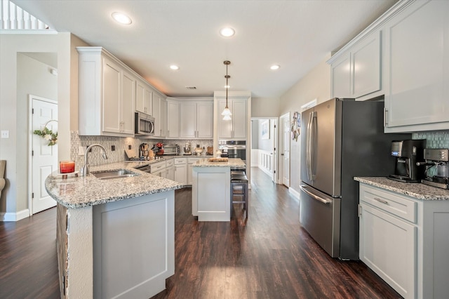 kitchen featuring a breakfast bar, sink, appliances with stainless steel finishes, decorative light fixtures, and light stone counters