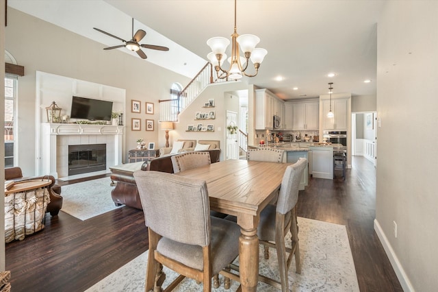 dining space with ceiling fan with notable chandelier, a fireplace, and dark wood-type flooring