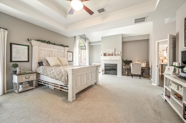 carpeted bedroom featuring ceiling fan, a raised ceiling, and a tile fireplace