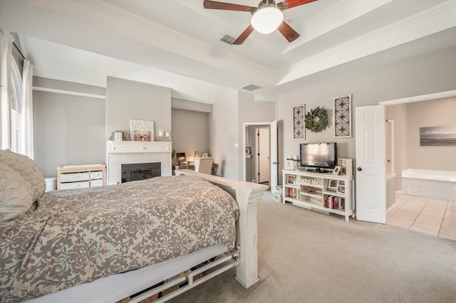 carpeted bedroom with ceiling fan, a tile fireplace, connected bathroom, and a tray ceiling