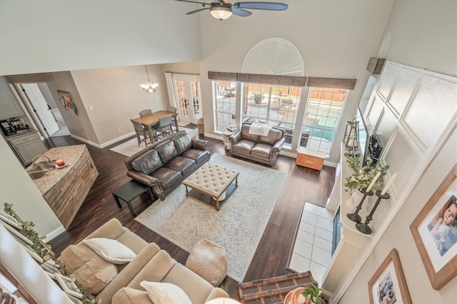 living room with ceiling fan with notable chandelier, dark hardwood / wood-style flooring, sink, and a high ceiling