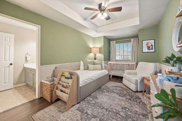 bedroom with a tray ceiling, connected bathroom, ceiling fan, and hardwood / wood-style floors