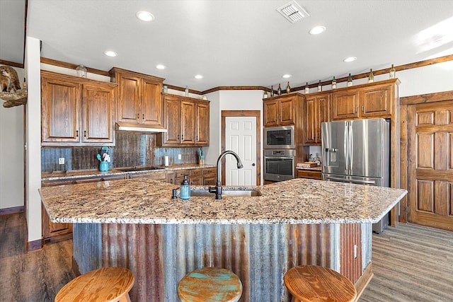 kitchen with an island with sink, stainless steel appliances, dark hardwood / wood-style floors, and ornamental molding