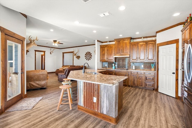 kitchen featuring a center island with sink, sink, light stone countertops, tasteful backsplash, and a kitchen bar