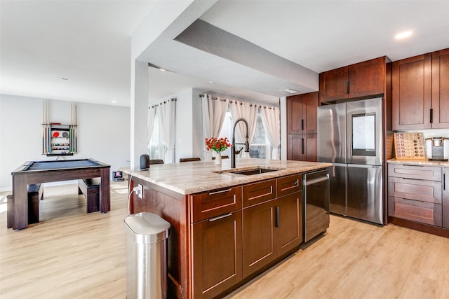 kitchen featuring stainless steel appliances, sink, billiards, light hardwood / wood-style floors, and an island with sink