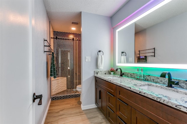 bathroom featuring a tile shower, wood-type flooring, a textured ceiling, toilet, and vanity