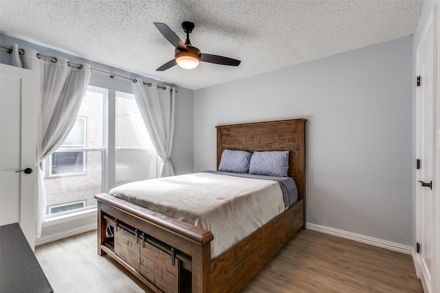 bedroom featuring a textured ceiling, ceiling fan, multiple windows, and light hardwood / wood-style flooring