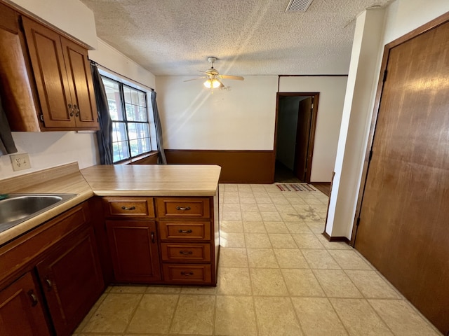 kitchen featuring ceiling fan, sink, kitchen peninsula, and a textured ceiling