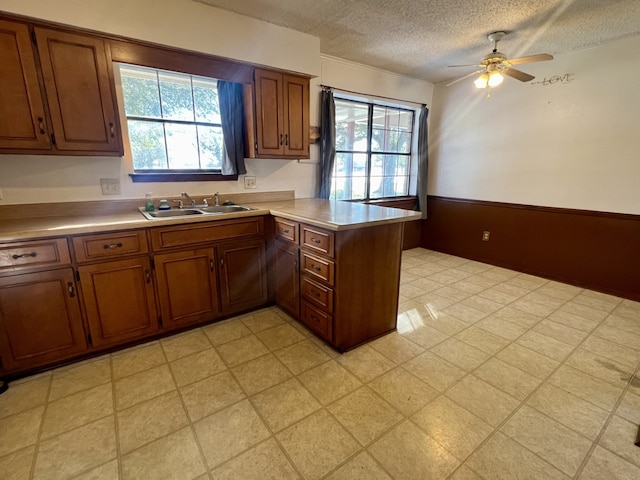 kitchen with a textured ceiling, plenty of natural light, kitchen peninsula, and sink