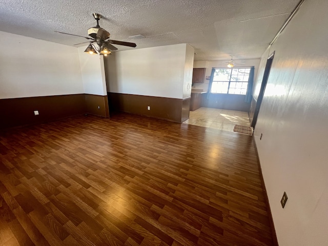 empty room featuring a textured ceiling, wooden walls, ceiling fan, and dark wood-type flooring