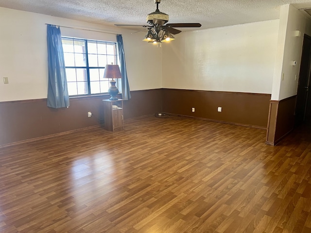 empty room with a textured ceiling, dark hardwood / wood-style floors, ceiling fan, and wooden walls