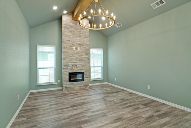 unfurnished living room with beamed ceiling, plenty of natural light, a notable chandelier, and a tiled fireplace