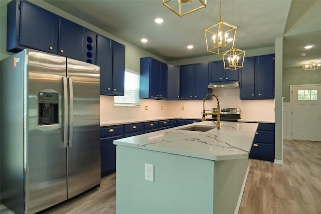 kitchen with stainless steel appliances, light stone counters, light hardwood / wood-style flooring, blue cabinets, and a kitchen island with sink