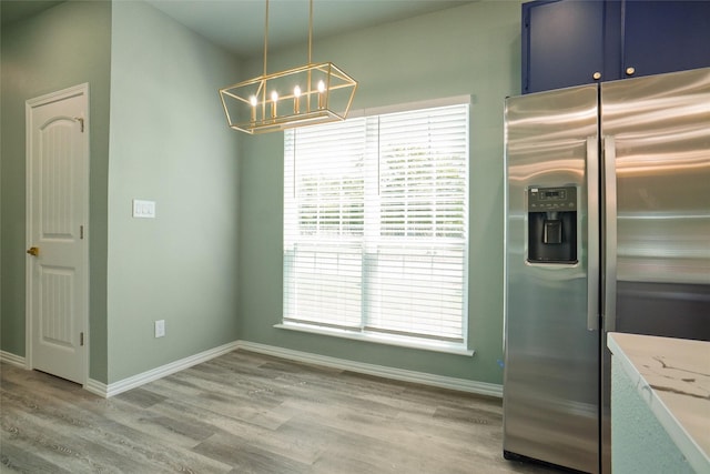 kitchen featuring light stone countertops, blue cabinetry, light hardwood / wood-style flooring, stainless steel fridge with ice dispenser, and hanging light fixtures