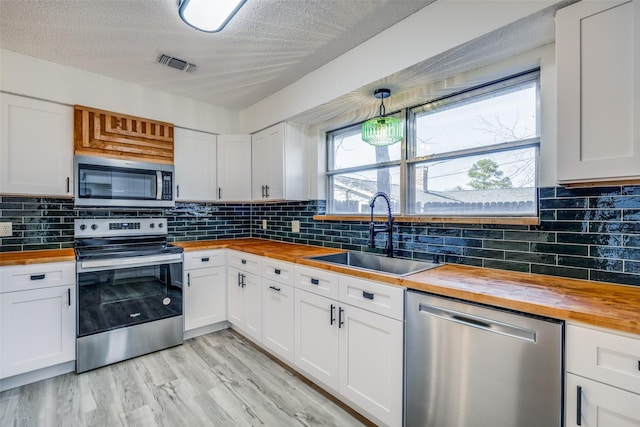 kitchen featuring appliances with stainless steel finishes, white cabinetry, sink, and butcher block counters