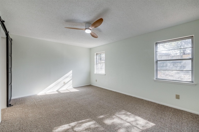 carpeted empty room featuring a textured ceiling, ceiling fan, and a barn door