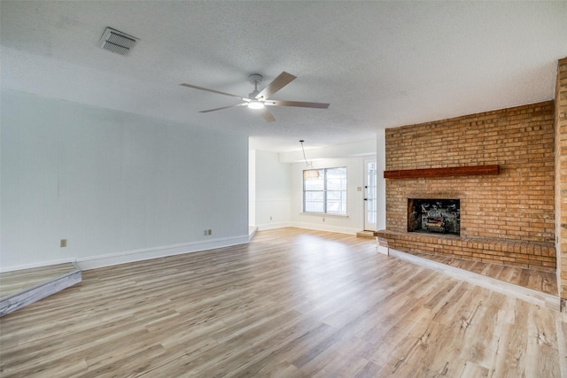 unfurnished living room with a textured ceiling, ceiling fan, light hardwood / wood-style floors, and a brick fireplace