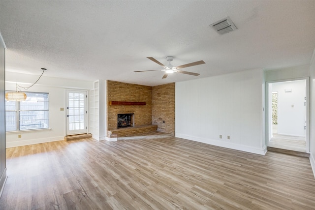 unfurnished living room with a textured ceiling, ceiling fan with notable chandelier, light hardwood / wood-style flooring, and a fireplace