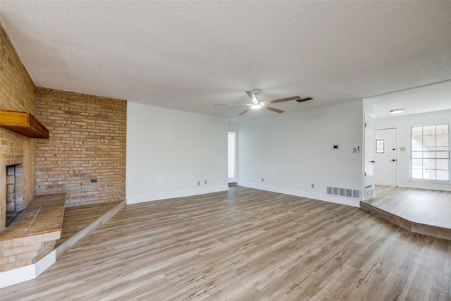 unfurnished living room featuring a brick fireplace, a textured ceiling, ceiling fan, and light hardwood / wood-style floors