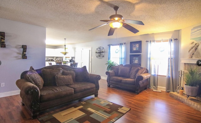 living room with dark hardwood / wood-style flooring, a textured ceiling, ceiling fan, and a brick fireplace